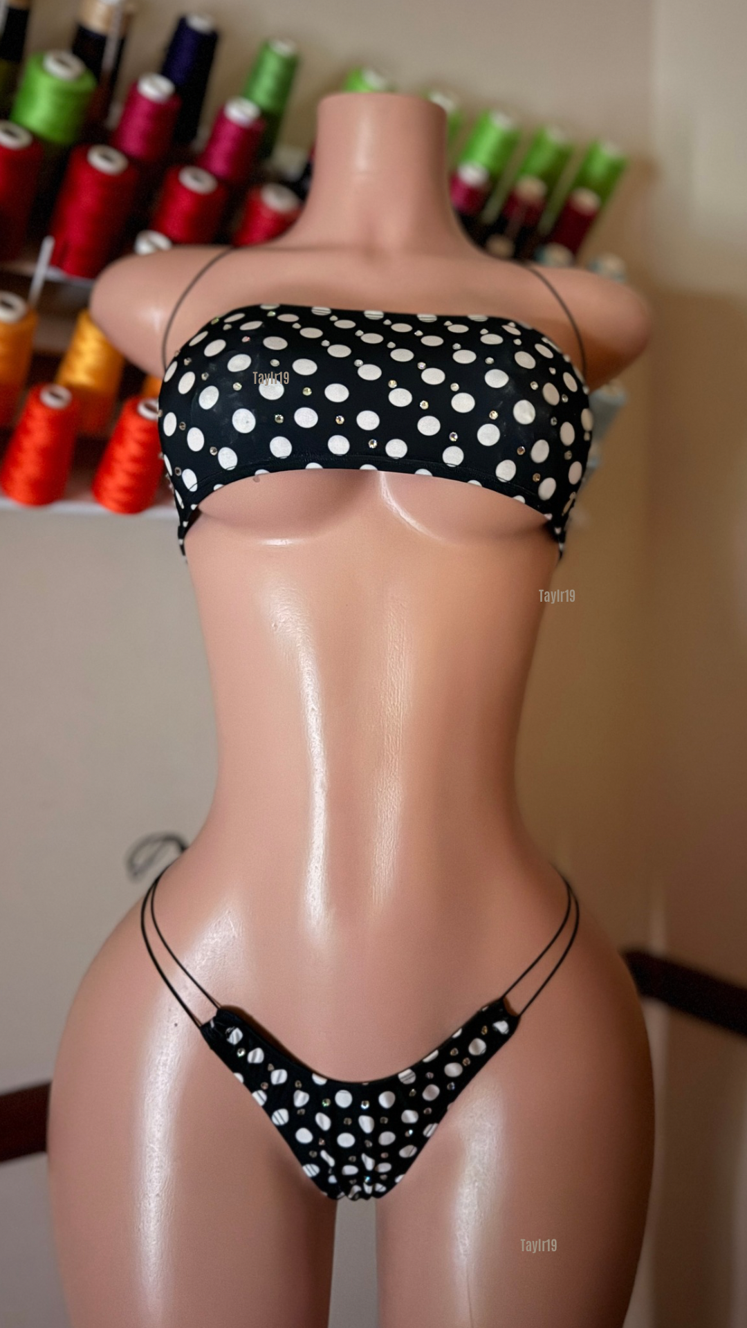 Mannequin wearing a black polka dot bikini with spools of thread in the background.