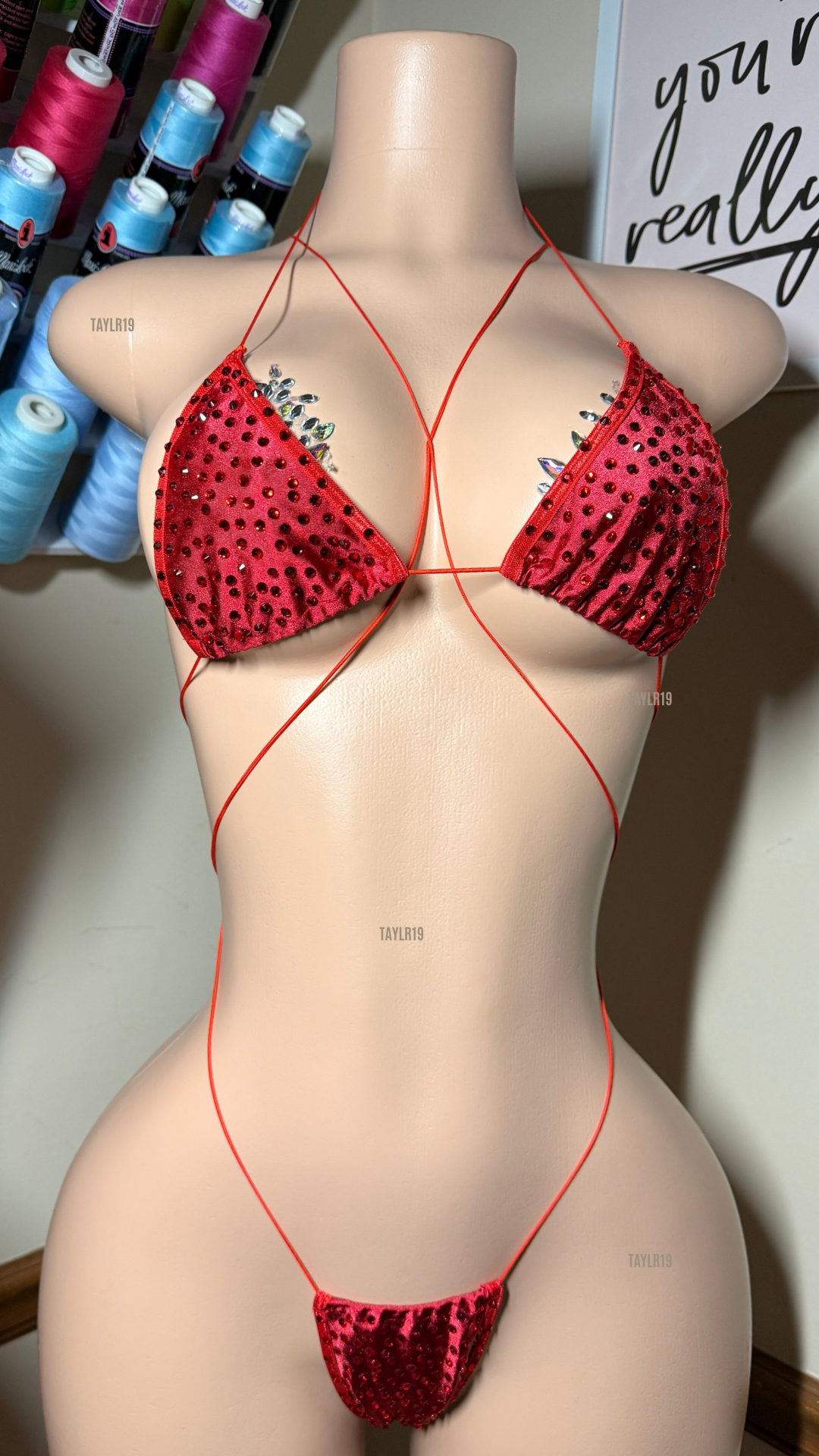 Front view of a rhinestone slingshot set on a mannequin, featuring a triangle top with jewel accents, thin crossing straps, and a minimal thong bottom.