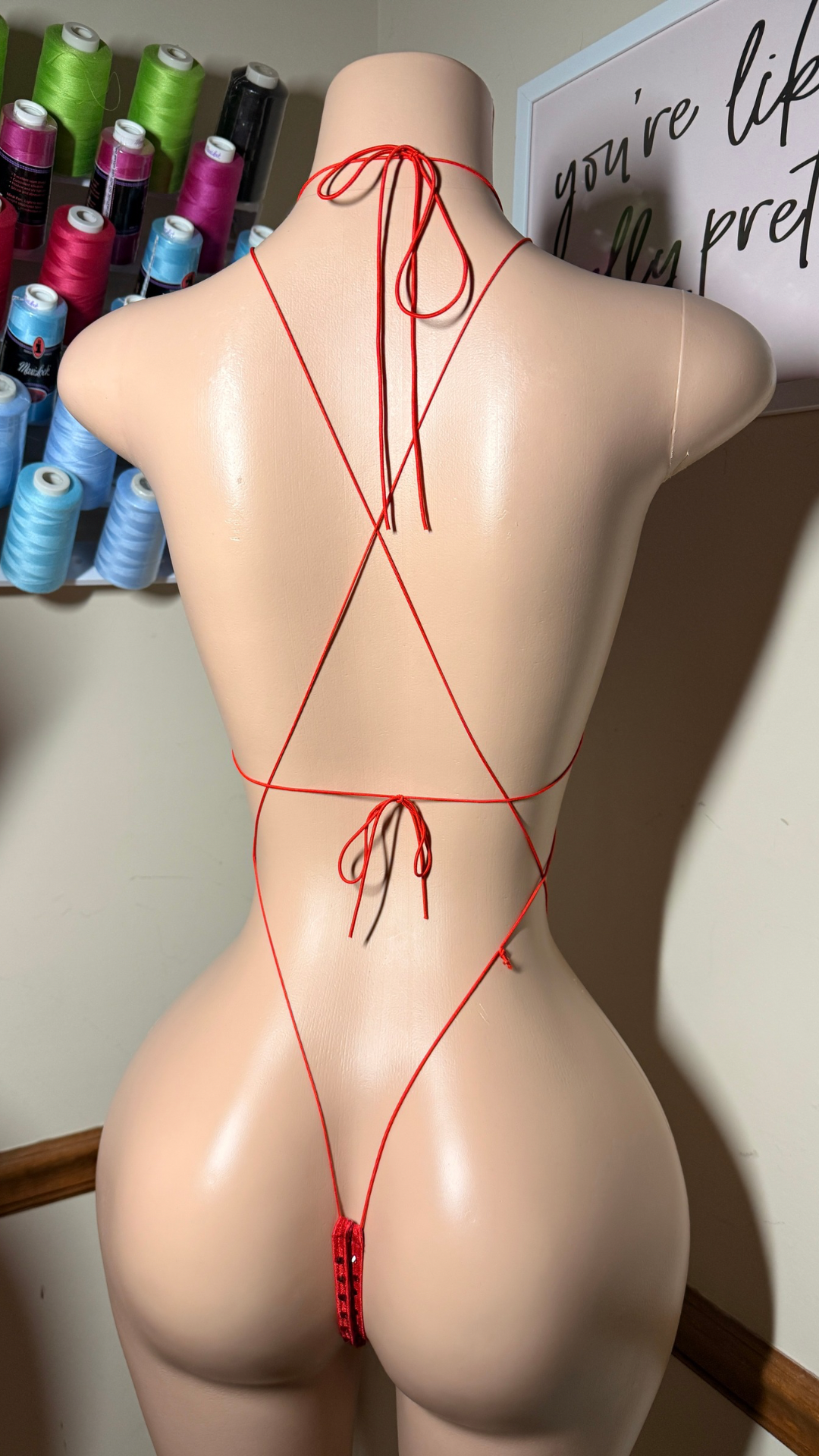 Back view of a rhinestone slingshot set on a mannequin, featuring a triangle top with jewel accents, thin crossing straps, and a minimal thong bottom.