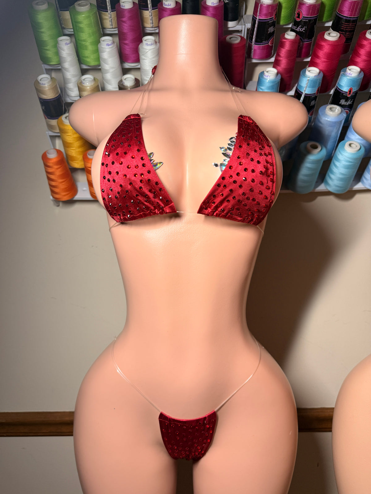 Red sequined bikini set displayed on a beige mannequin torso, with a background of colorful spools of thread.
