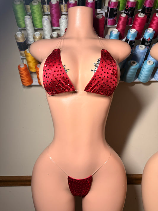 Red sequined bikini set displayed on a beige mannequin torso, with a background of colorful spools of thread.